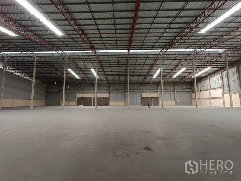 Factory for rent in Samut Prakan - Wide industrial hall showing tall columns, metal roof panels and long LED light strips suitable for production or storage operations.