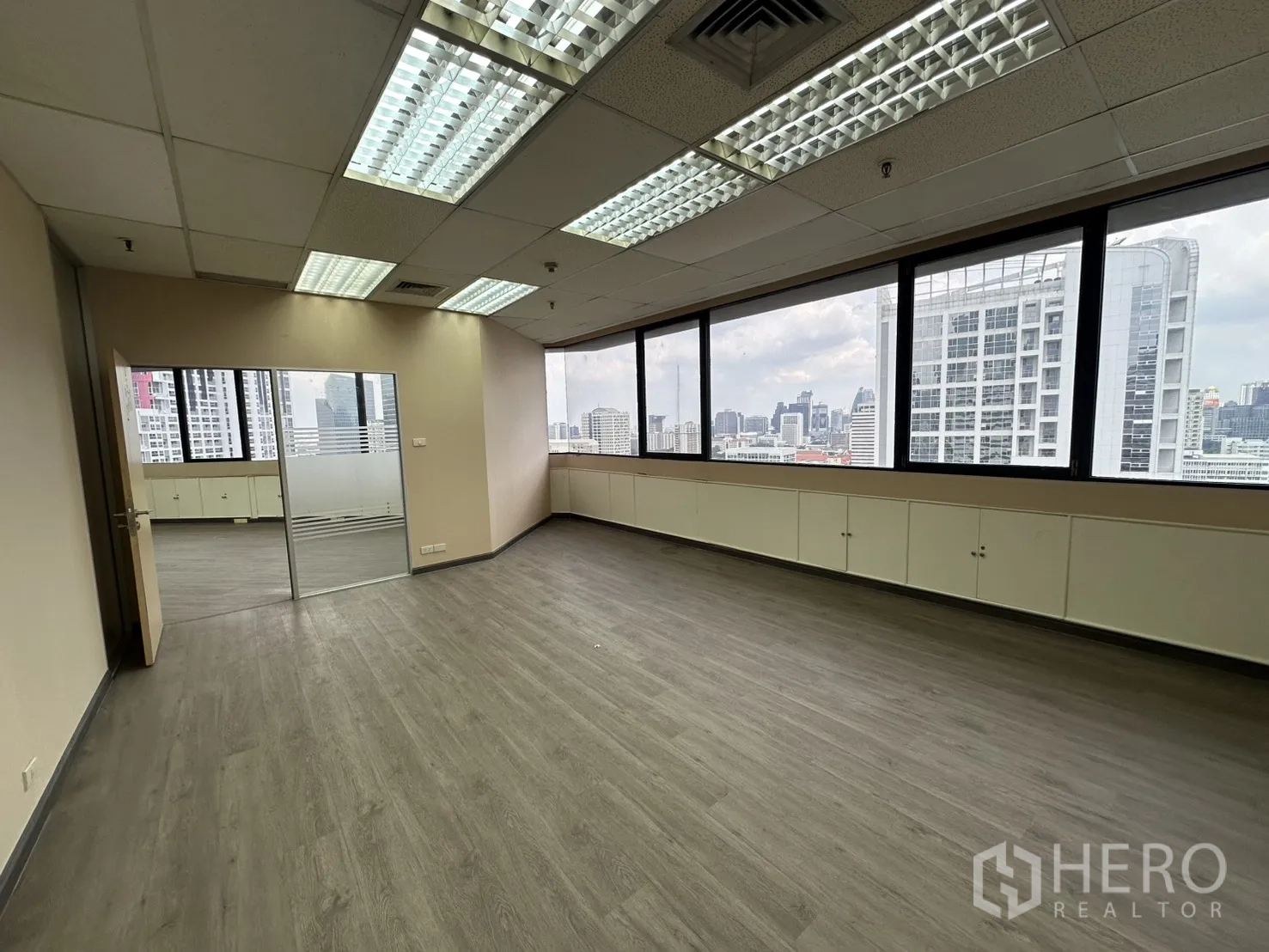 Office Space for rent in Bang Rak, Bangkok - Corner office with wide windows, wood-look floors and Bangkok skyline views.