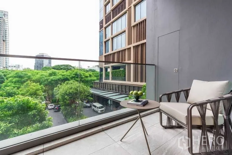 Condominium for rent in Pathum Wan, Bangkok - Private balcony with glass railing, lounge chair, and views of trees and modern buildings.