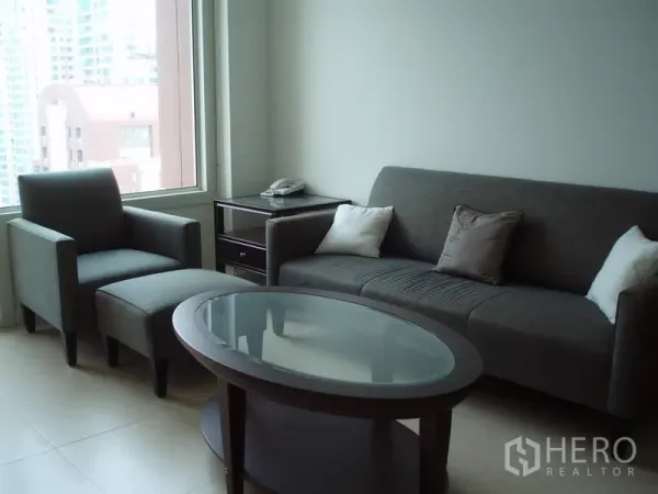 公寓 出租在Ratchathewi, Bangkok - 明亮客厅，灰色沙发与玻璃茶几，大窗欣赏城市景观，曼谷拉差贴威一居公寓。