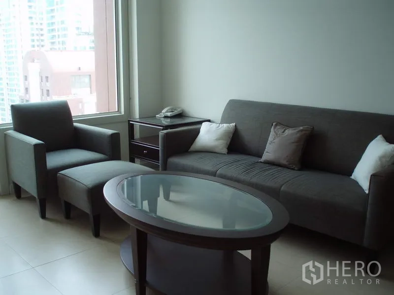 公寓 出租在Ratchathewi, Bangkok - 明亮客厅，灰色沙发与玻璃茶几，大窗欣赏城市景观，曼谷拉差贴威一居公寓。
