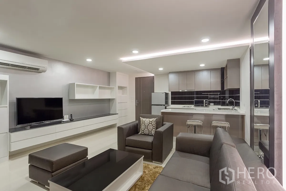 Condominium for rent in Khlong Toei, Bangkok - Open-plan living area with sofa set, TV console, built-in shelving, and adjoining kitchen.