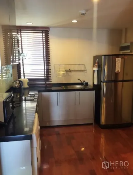 Condominium for rent in Pathum Wan, Bangkok - Modern kitchen with black stone countertops, stainless-steel fridge and electric hob.