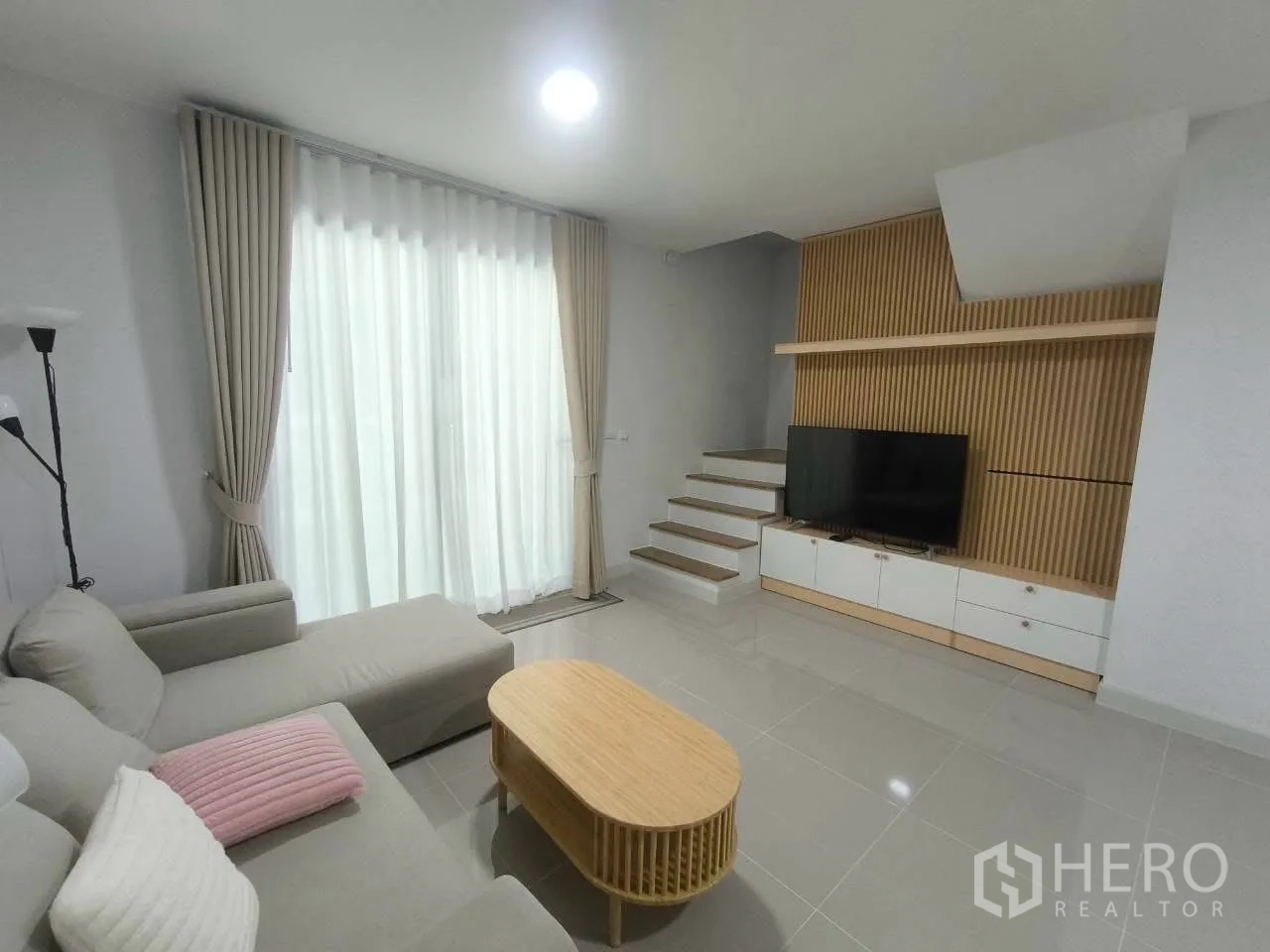 联排别墅 for rent in Bang Phli, Samut Prakan - 明亮客厅，转角沙发、落地窗帘与电视墙。