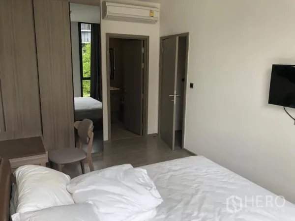 คอนโด ให้เช่าในWatthana, Bangkok - มุมห้องนอนใหญ่ไปยังตู้เสื้อผ้า โต๊ะทำงาน ทีวีติดผนัง และทางเข้าห้องน้ำในตัว