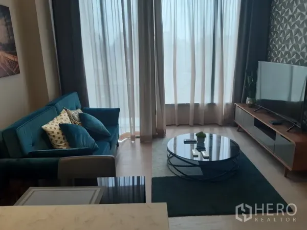 公寓 出租或出售在Watthana, Bangkok - 明亮客厅，纱帘、青绿色沙发、圆形玻璃茶几与影音柜。