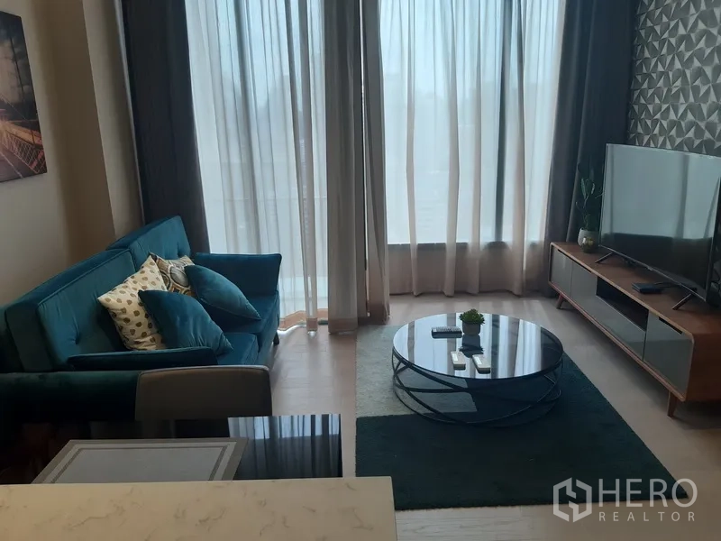 公寓 出租或出售在Watthana, Bangkok - 明亮客厅，纱帘、青绿色沙发、圆形玻璃茶几与影音柜。