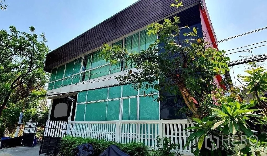 Home Office for rent or sale in Bang Khun Thian, Bangkok - Angled view of the glass-fronted building surrounded by lush greenery.