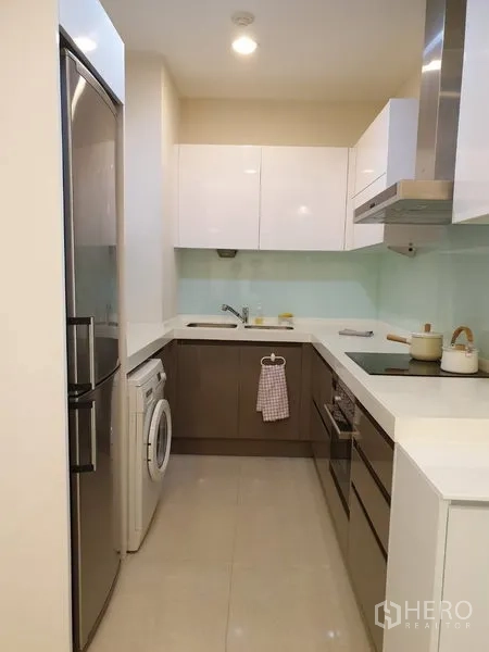公寓 出租在Pathum Wan, Bangkok - 现代U形厨房，亮面柜体，灶台、抽油烟机、冰箱与室内洗衣机。