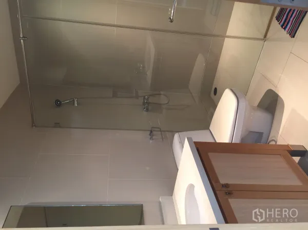 Condominium for rent or sale in Khlong Toei, Bangkok - Contemporary bathroom with glass-enclosed shower, toilet and vanity.