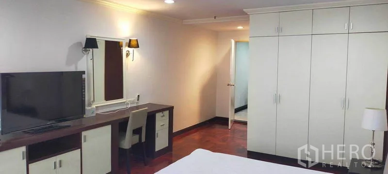 Condominium for rent in Watthana, Bangkok - Master bedroom with TV console, fitted wardrobes, and wood flooring.