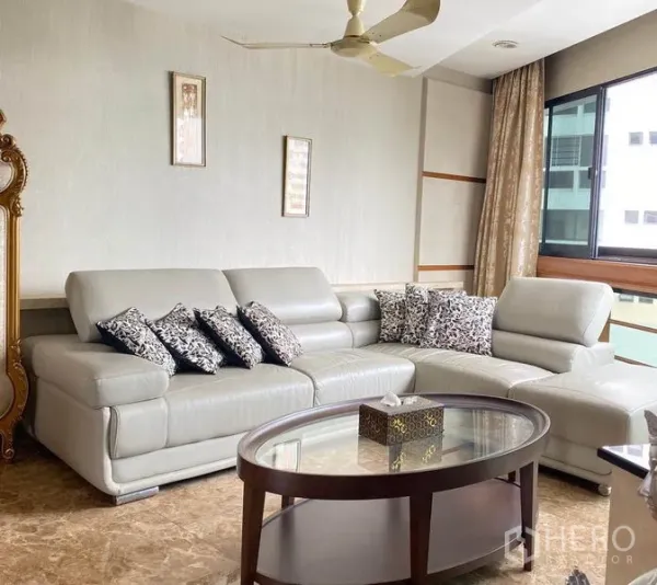 Condominium for rent in Khlong Toei, Bangkok - Bright lounge corner with L-shaped leather sofa, ceiling fan and large window.