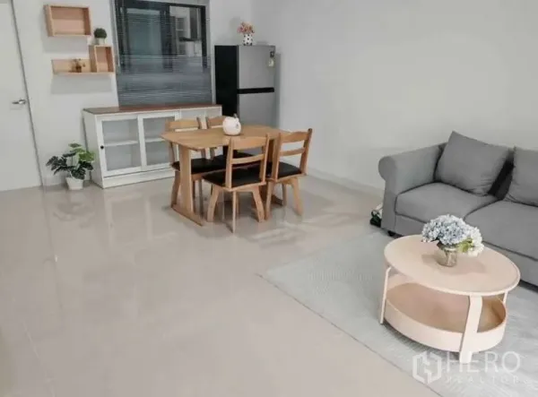 Townhouse for rent in Bang Phli, Samut Prakan - Open-plan living and dining room with grey sofa, wooden dining set and refrigerator.