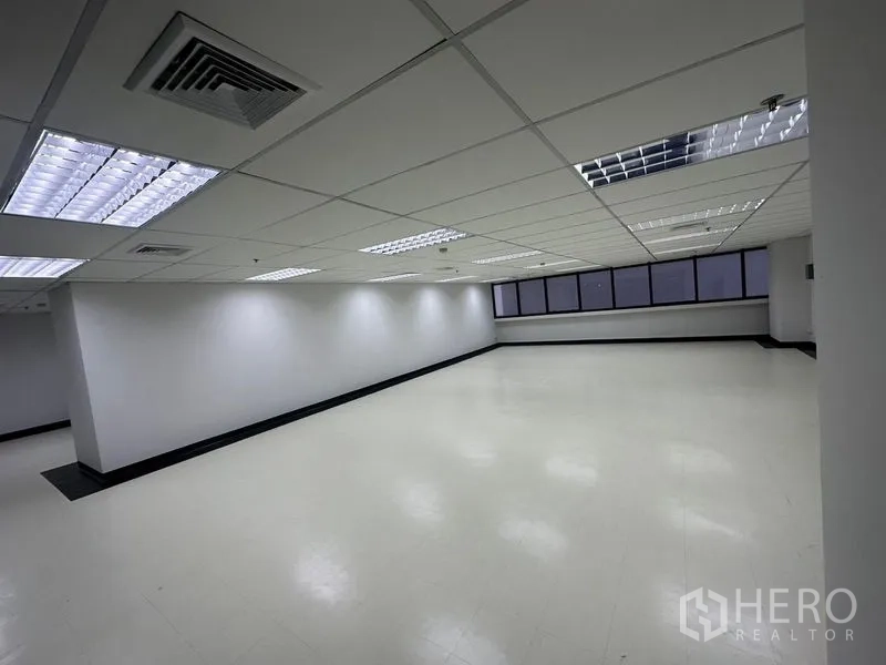 สำนักงาน ให้เช่า - โถงสำนักงานกว้าง พื้นโทนอ่อน โคมไฟตะแกรงและแนวหน้าต่างยาวรับแสงธรรมชาติ