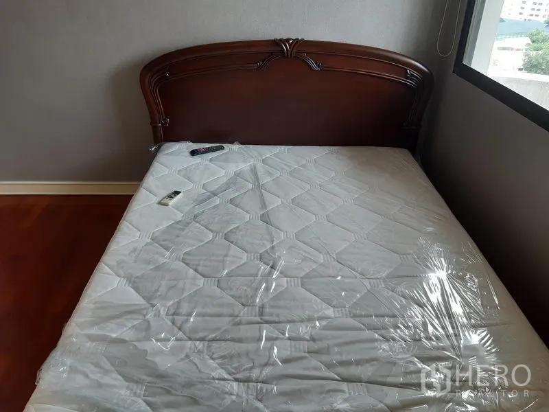 Condominium for rent in Khlong Toei, Bangkok - Compact bedroom with wooden headboard, new mattress and natural light from the window.
