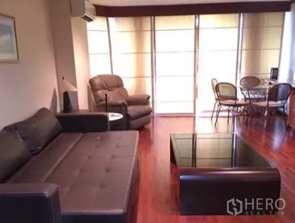 公寓 出租或出售在Watthana, Bangkok - 客厅配皮沙发、玻璃茶几与窗边用餐角。