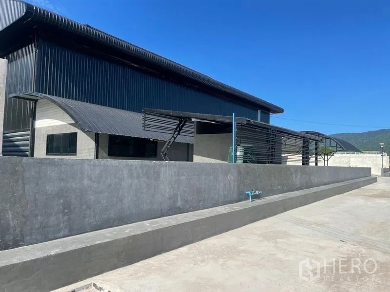 货栈 出租在Ban Bueng, Chon Buri - 钢板外墙仓库侧立面，长装卸平台，远处可见山景。