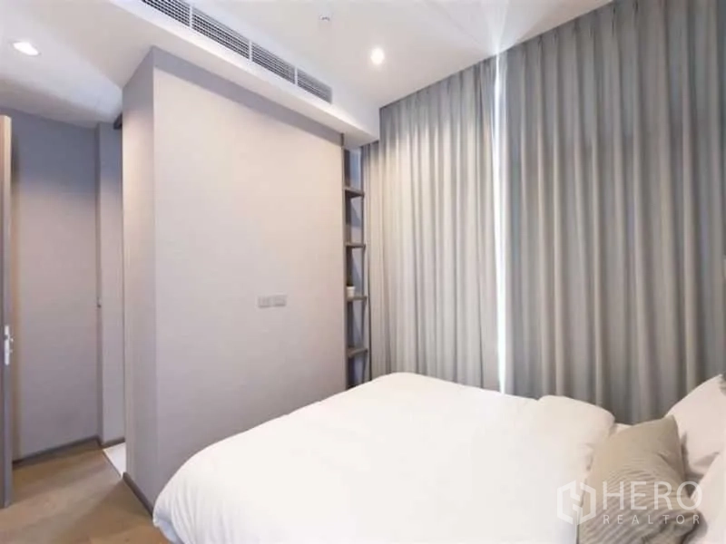 公寓 出租在Bang Rak, Bangkok - 卧室另一角度，可见落地窗帘与门旁的窄型嵌入式搁架。