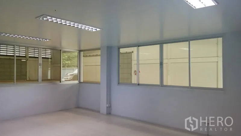 Warehouse for rent in Si Racha, Chon Buri - Clean office room with large windows overlooking the warehouse and fluorescent lighting.