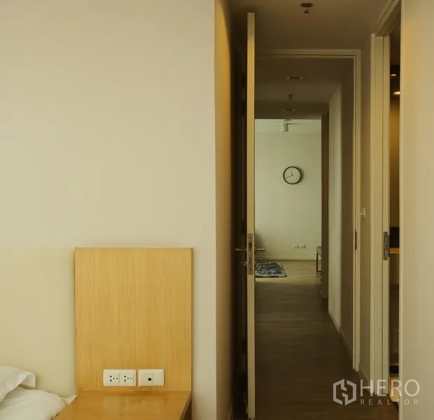Condominium for rent in Bang Rak, Bangkok - Hallway from bedroom to living room with wood floors and wall clock.