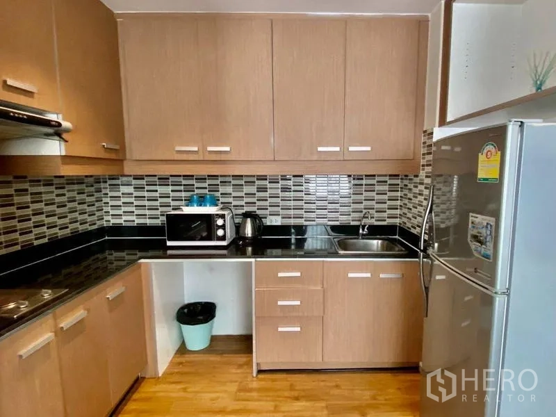 Condominium for rent in Khlong Toei, Bangkok - L-shaped kitchen with wood cabinets, mosaic backsplash, black stone counters and stainless refrigerator.