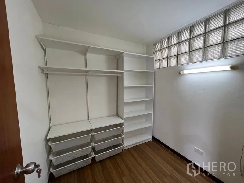 Townhouse for rent or sale in Suan Luang, Bangkok - Walk-in closet fitted with white shelving and drawers beside a glass-block window.