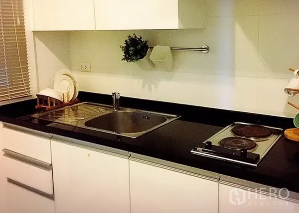 Condominium for rent in Khlong Toei, Bangkok - Compact kitchen with black stone countertop, sink and electric hob.