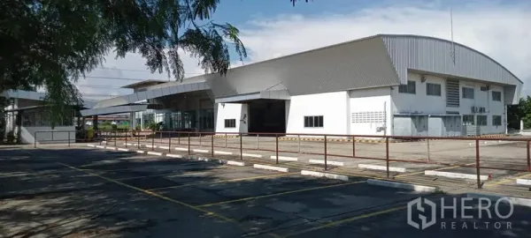 Warehouse for rent or sale in Lam Luk Ka, Pathum Thani - Wide exterior view of a modern metal-roofed warehouse with large paved yard and marked parking bays.