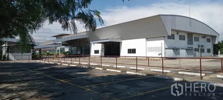 Warehouse for rent or sale in Lam Luk Ka, Pathum Thani - Wide exterior view of a modern metal-roofed warehouse with large paved yard and marked parking bays.
