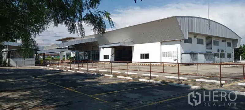 Warehouse for rent or sale in Lam Luk Ka, Pathum Thani - Wide exterior view of a modern metal-roofed warehouse with large paved yard and marked parking bays.