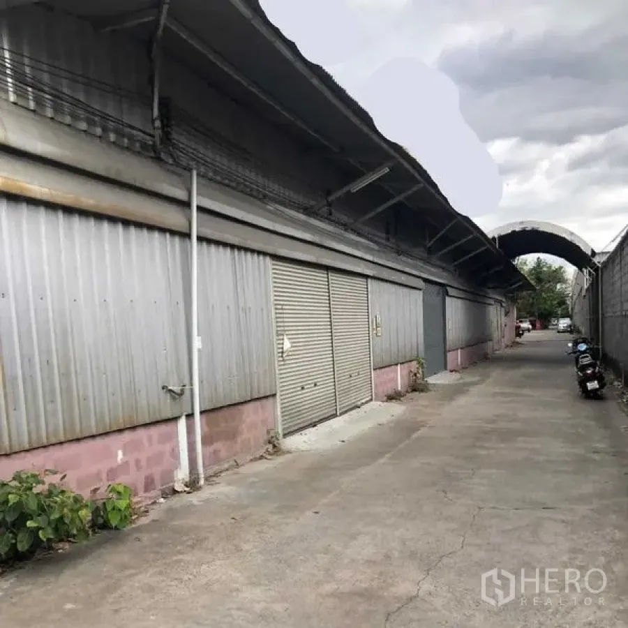 Warehouse for rent in Khan Na Yao, Bangkok - Corrugated steel warehouse exterior with roller shutter doors along a 5‑meter access lane.