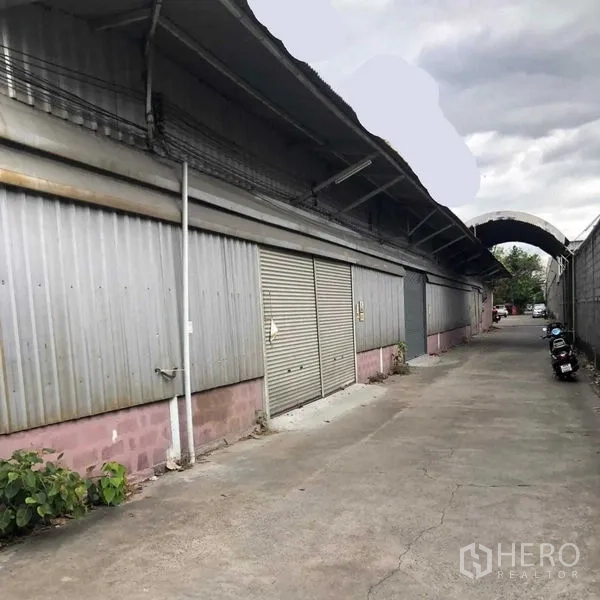 Warehouse for rent in Khan Na Yao, Bangkok - Corrugated steel warehouse exterior with roller shutter doors along a 5‑meter access lane.