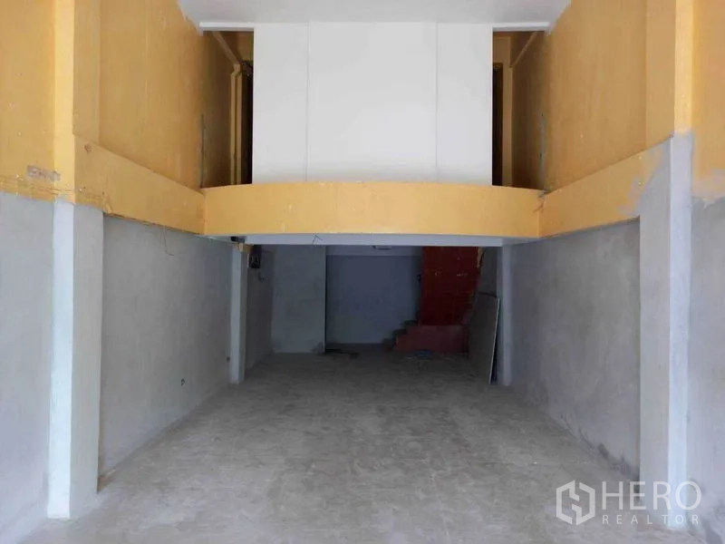Shophouse for rent in Watthana, Bangkok - Empty ground-floor shop space with high ceiling, mezzanine and concrete floor.