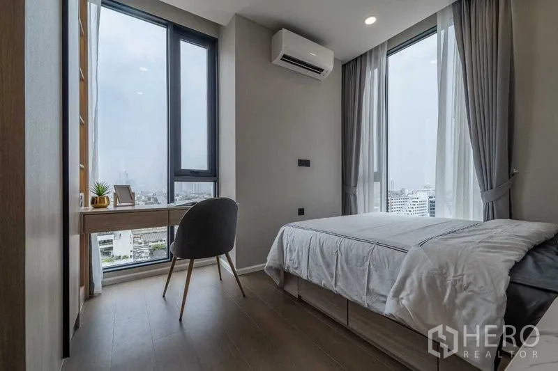 Condominium for rent in Pathum Wan, Bangkok - Second bedroom with single bed, corner desk and wraparound windows with city views.