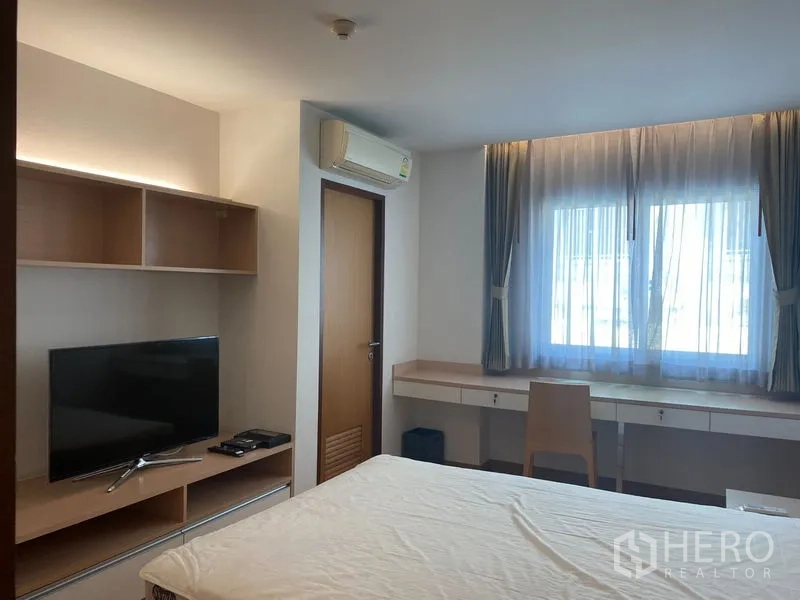 Condominium for rent or sale in Khlong Toei, Bangkok - Bedroom with TV and shelving, air conditioning and an extended study desk by the window.