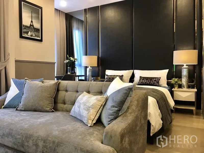 Condominium for rent in Watthana, Bangkok - Studio-style sleeping zone with dark feature wall, bedside lamps and a tufted fabric sofa.