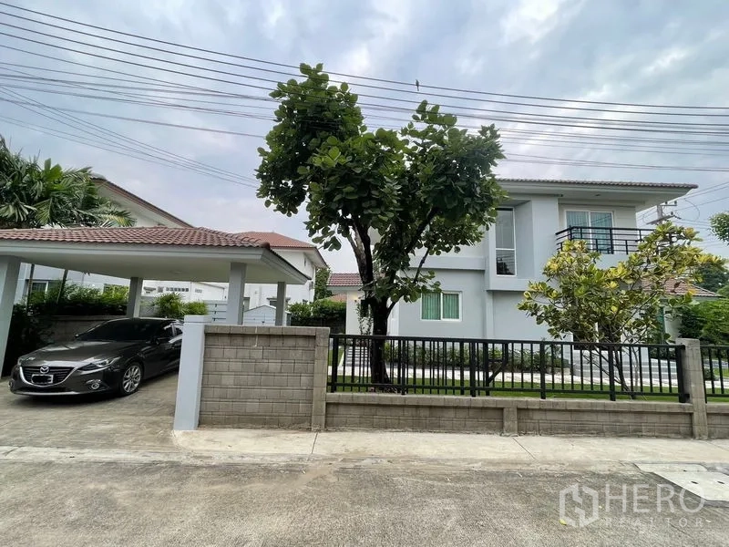Detached House for sale in Lam Luk Ka, Pathum Thani - Two-storey detached house with carport, front fence and a mature tree on a quiet lane.