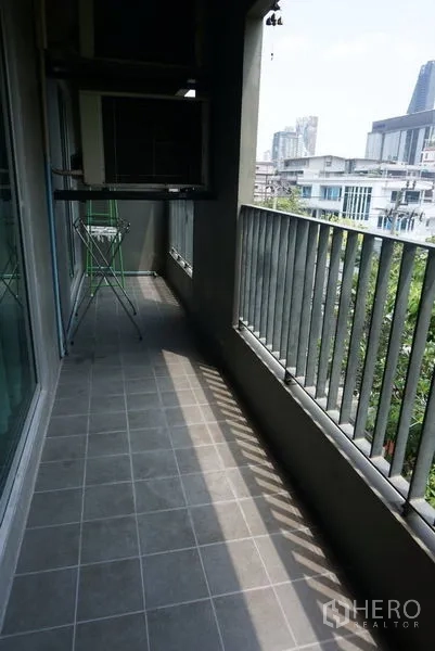 Condominium for sale in Khlong Toei, Bangkok - Long covered balcony with tiled floor and metal railings, ideal for outdoor seating.
