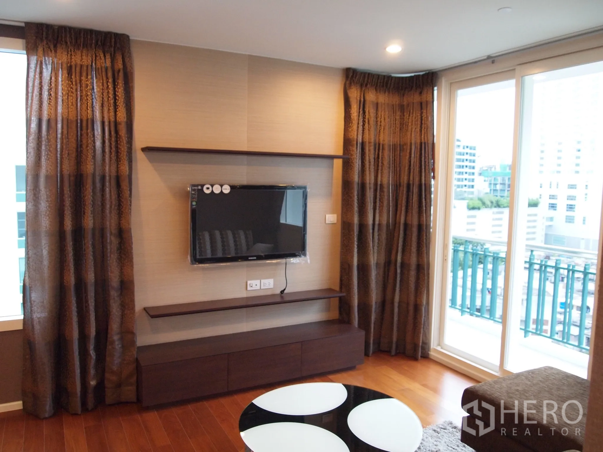 Condominium for rent or sale in Watthana, Bangkok - Living room with wall-mounted TV, sliding doors to a city-view balcony at Wind Sukhumvit 23.