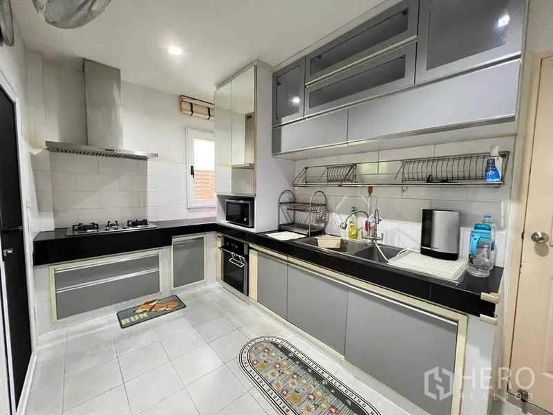 Detached House for sale in Bang Kruai, Nonthaburi - Modern L-shaped kitchen with gas hob, hood, grey cabinetry, and black countertops.
