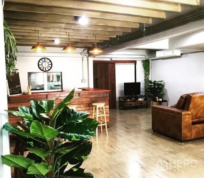 Townhouse for rent in Chatuchak, Bangkok - Spacious living room with leather sofa, TV corner, wood floors and greenery.