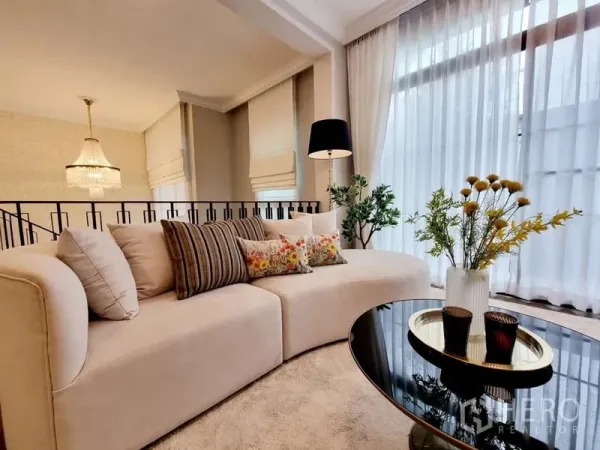 Detached House for rent in Saphan Sung, Bangkok - Bright lounge with curved cream sofa, floor lamp, sheer curtains, and glass coffee table with flowers.