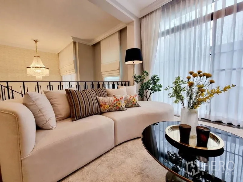Detached House for rent in Saphan Sung, Bangkok - Bright lounge with curved cream sofa, floor lamp, sheer curtains, and glass coffee table with flowers.