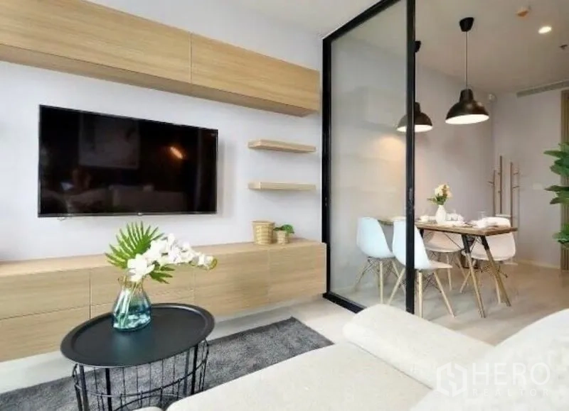 Condominium for rent in Pathum Wan, Bangkok - Living room with floating shelves, TV wall, and glass door leading to the dining area.