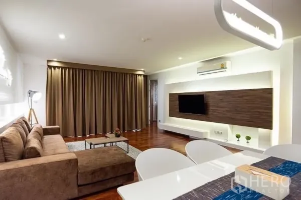 公寓 出租在Pathum Wan, Bangkok - 客厅朝向影音墙，壁挂电视、棕色沙发与就餐区一体。