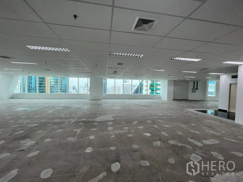 สำนักงาน ให้เช่า - ชั้นสำนักงานโอเพ่นเพลนกว้าง เพดานตะแกรงพร้อมไฟ และหน้าต่างบานใหญ่เห็นวิวสกายไลน์กรุงเทพฯ