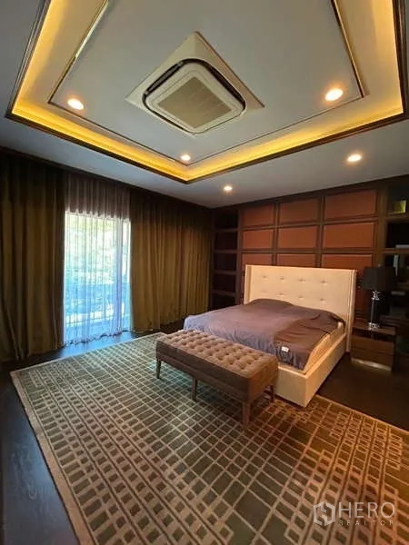 Detached House for rent in Bang Kapi, Bangkok - Large bedroom with tufted headboard, bench, big rug, and sliding door to balcony.