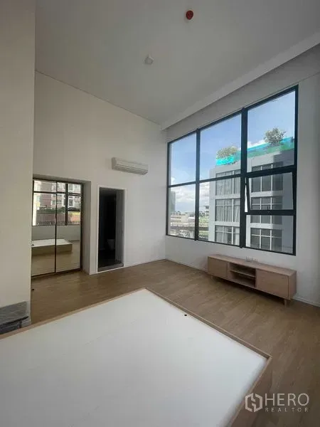 Condominium for rent in Khlong Toei, Bangkok - Spacious double-height living room with large windows, wall-mounted air conditioner and media console.