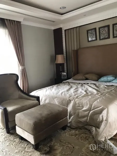 Townhouse for rent or sale in Bang Kho Laem, Bangkok - Master bedroom featuring upholstered headboard, armchair with ottoman, soft carpet and large window.
