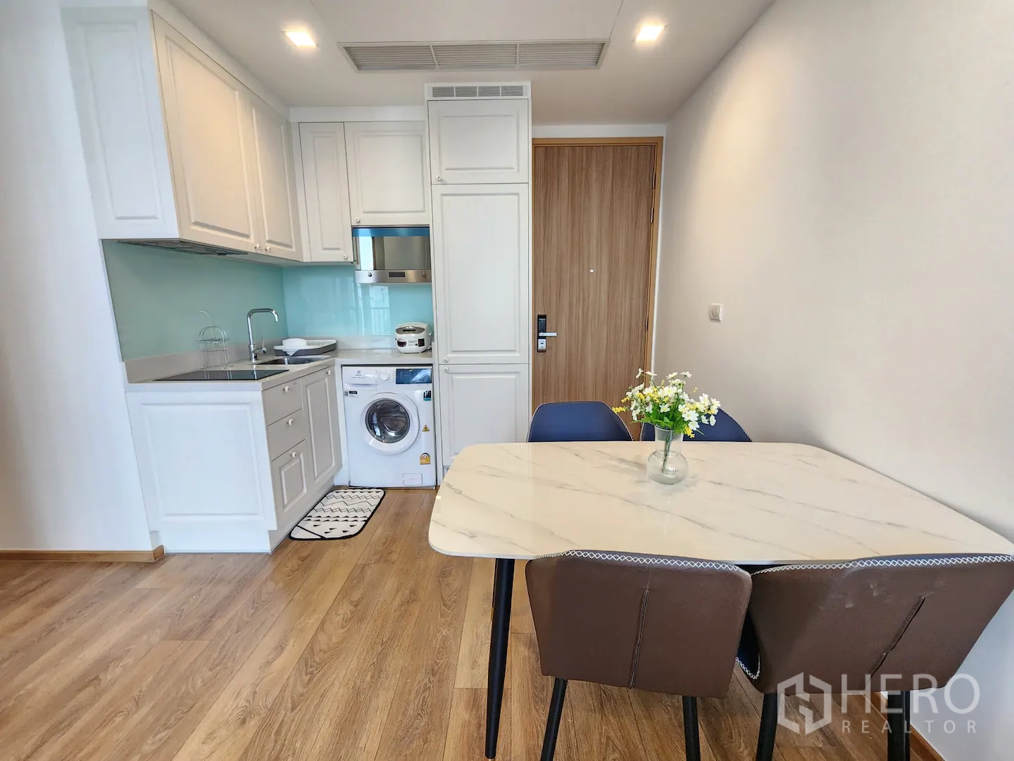 Condominium for rent in Watthana, Bangkok - Open kitchenette and dining area with white cabinetry, washer, induction hob and marble-top table.